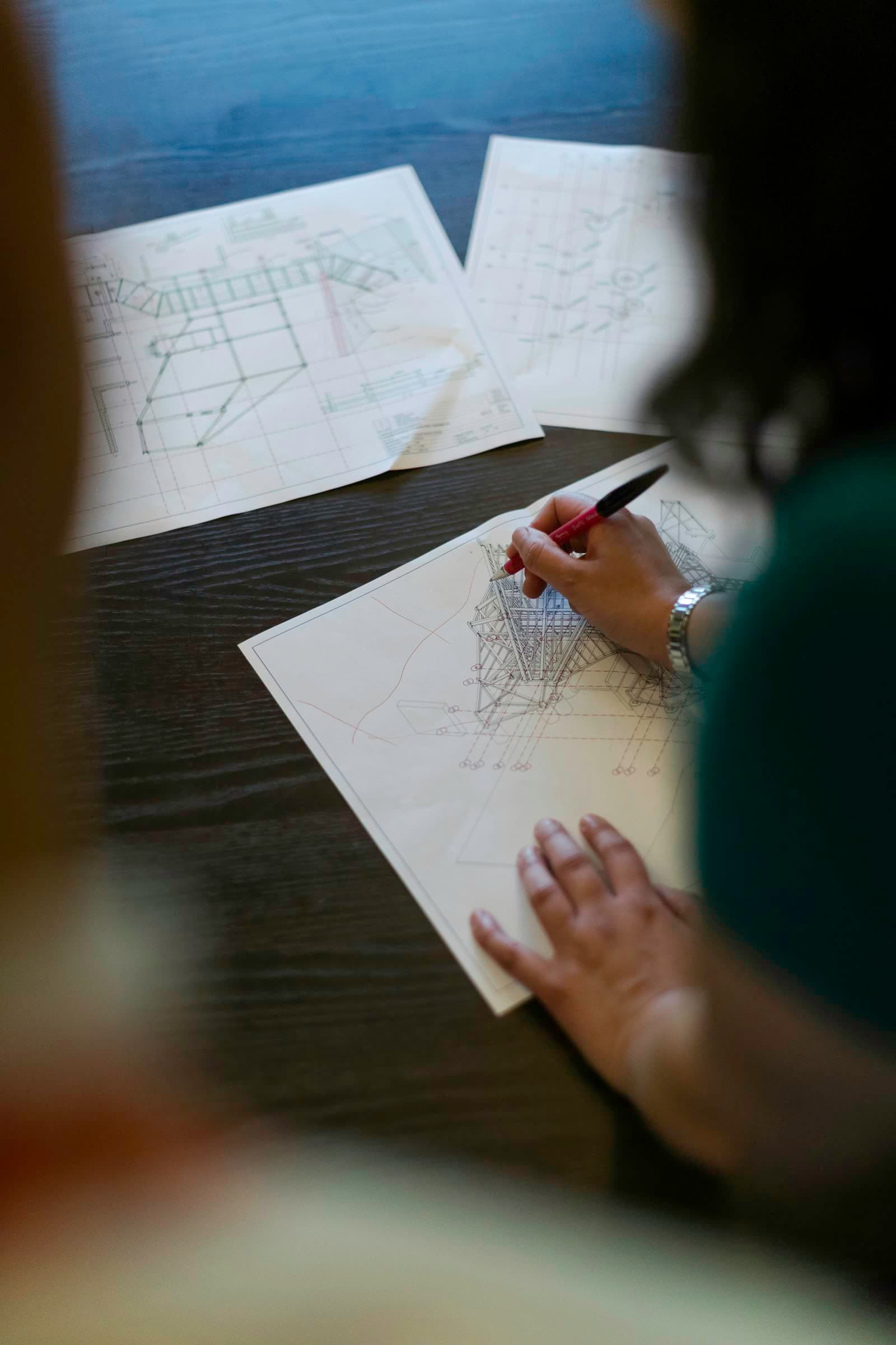 Profesional revisando y marcando a mano planos estructurales sobre una mesa de trabajo